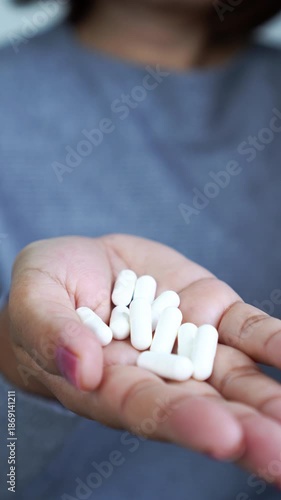vertical video woman's hand holding white capsule pills or supplements. Concept of medication, healthcare treatment, pharmacy, painkiller dosage, and medical care for illness at home