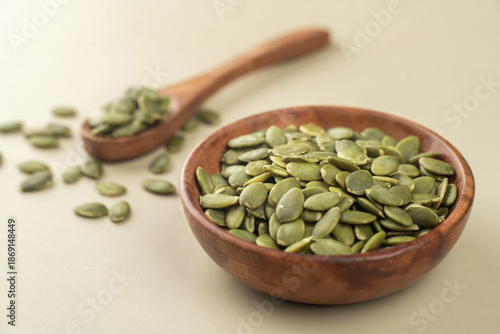 Green Pumpkin seeds in a wooden bowl placed on a beige background.