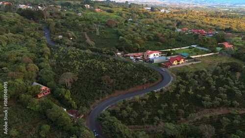 Aerial pull-back shot of a winding mountain road and lush coffee plantations with traditional houses in San Rafael, Heredia, Costa Rica at sunset