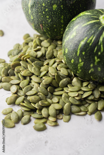 Green Pumpkin seeds in a wooden bowl, along with green baby pumpkin, placed on a textured background.