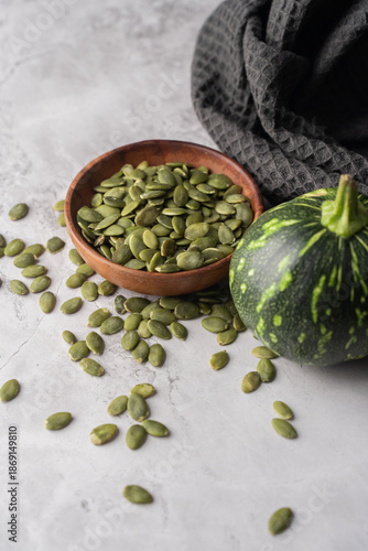 Green Pumpkin seeds in a wooden bowl, along with green baby pumpkin, placed on a textured background.