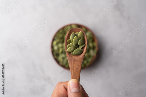 Green Pumpkin seeds in a wooden spoon placed on a textured background.