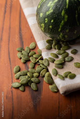 Green Pumpkin seeds, along with a baby pumpkin, placed on a textured background.