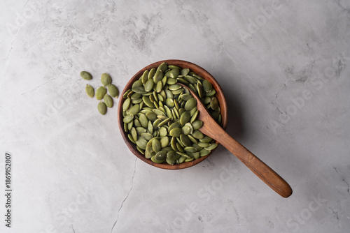 Green Pumpkin seeds in a wooden bowl placed on a textured background.