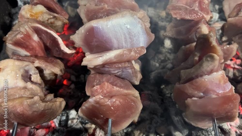 A close-up shot of meat being grilled. Pieces of meat are strung on metal skewers.