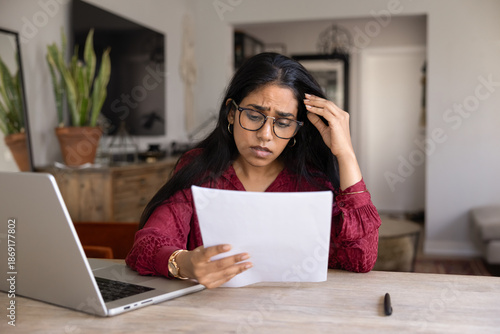 Foto Frustrated concerned young Indian woman in glasses reading bad news in legal doc