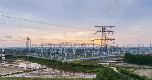 Wallpaper Mural Aerial time-lapse of a large power substation at dawn, with high-voltage towers and transmission lines silhouetted against a soft morning sky over rural farmland.   Torontodigital.ca