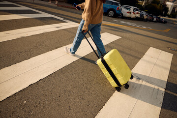Woman is crossing the street dragging a suitcase