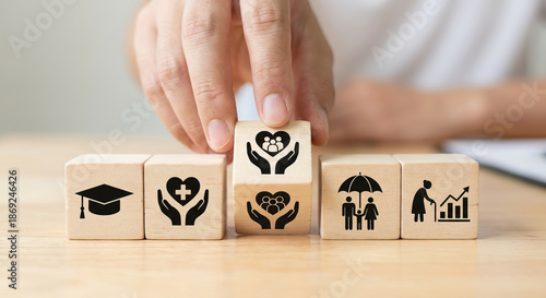 Hand arranging wooden blocks with icons symbolizing social care, health, education, insurance, and retirement planning