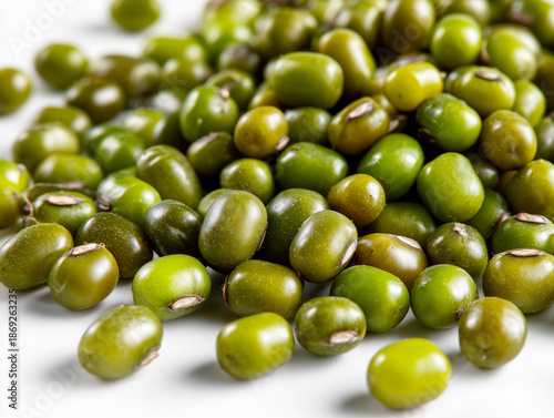 A close-up, high-angle view of a pile of raw, dried mung beans (Vigna radiata), also known as green gram, scattered on a plain white background. 