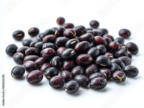 A close-up, high-angle view of a pile of raw, dried black beans, which appear to be black turtle beans (Phaseolus vulgaris), scattered on a plain white background. 