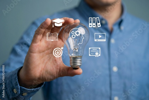 Educator holding a glowing lightbulb hologram with learning symbols to promote innovative e-learning solutions, enhance knowledge sharing, and develop creative educational strategies for future genera