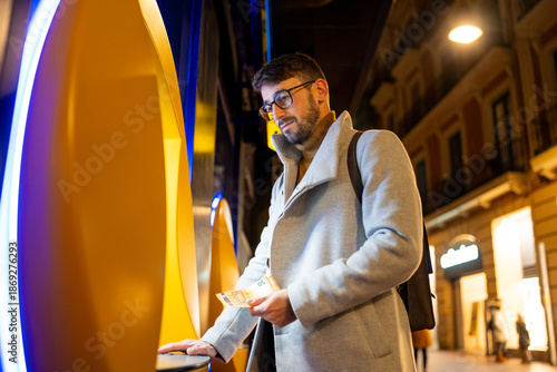 Bilde på lerret Young businessman withdrawing money from atm at night