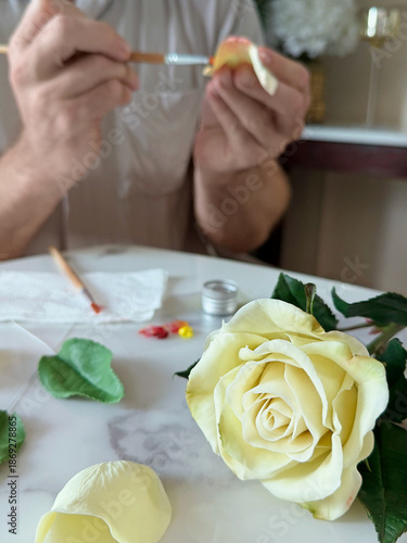 Bright conceptual photo of a muscular bearded man painting, gluing and assembling a flower made of air dry clay. Creative handmade process and art workshop concept, Vertical, focus on flower