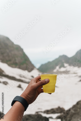Hiker holding yellow cup in snowy mountain landscape during trekking break