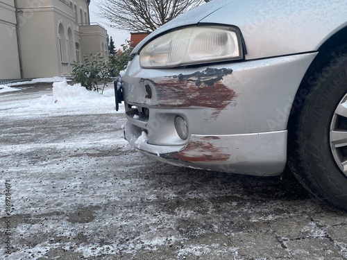 Wallpaper Mural Beschädigte Stoßstange eines Autos mit Kratzern und Lackschäden auf vereister Straße im Winter. Das Motiv steht für Verkehrsunfall, Sachschaden, Glätte und winterliche Fahrbedingungen. Torontodigital.ca