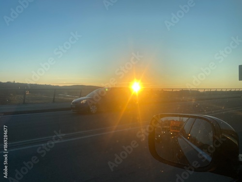 Wallpaper Mural ief stehende Sonne blendet den Fahrer auf einer Straße während der Fahrt. Das Motiv steht für Verkehr, Sonnenblendung, Sicherheit, Pendeln und Abendstimmung unterwegs. Torontodigital.ca