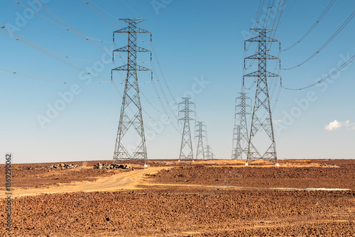 Desert transmission towers stretch across arid landscape under clear blue sky