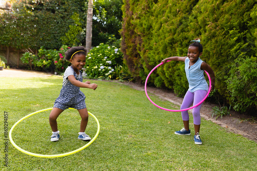 Full length of cheerful african american sisters enjoying with plastic hoops at garden