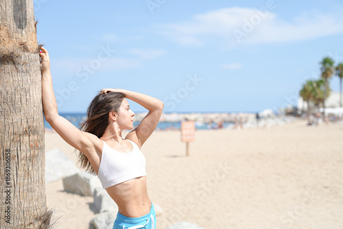 Photography A woman is posing on a beach with a palm tree behind her