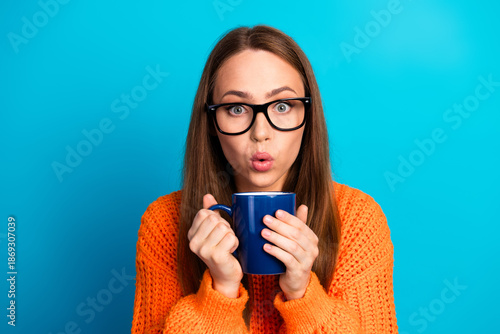 Tableau sur toile Young woman in orange sweater sipping coffee in blue studio background