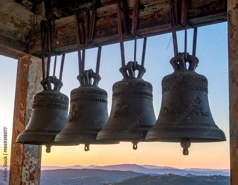 Obraz premium Four aged bronze bells hang, overlooking a hazy mountain vista