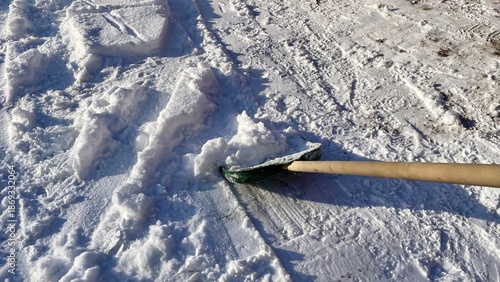 Man clearing fresh white snow with a green shovel in winter courtyard, close up of snow removal process
