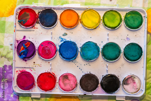 Colorful photo of a watercolor box lying on a table and used to paint watercolors on canvas.