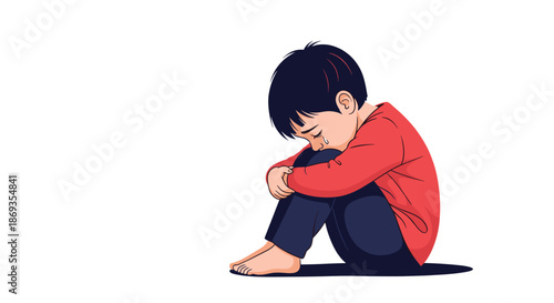 Lonely and sad young boy in a red shirt sitting on the floor with his head tucked into his knees while crying alone.