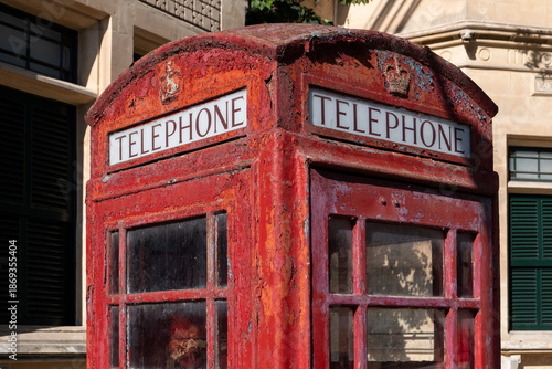 Weathered red telephone booth standing in a Mediterranean street, vintage urban element contrasting with historic stone architecture.