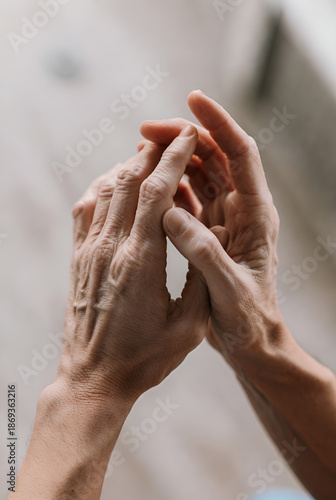 close-up view of a person's hands. The hands appear to be clasped together, with the fingers intertwined, suggesting a gesture of prayer, contemplation, or deep thought. The background is blurred, kee
