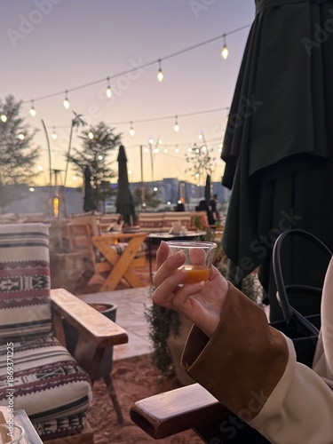 A girl holding a cup of Saudi Arabian coffee with a background of embroidered seats. Traditional Diamonds Folk Sadu Arabian Hand Weaving Pattern
