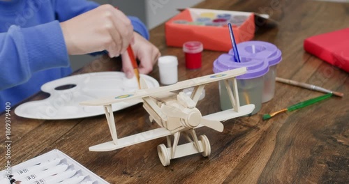 Little boy hands mix paints on palette near wooden toy airplane at desk closeup. Talented child prepares colors for old aircraft model at art class. Creativity