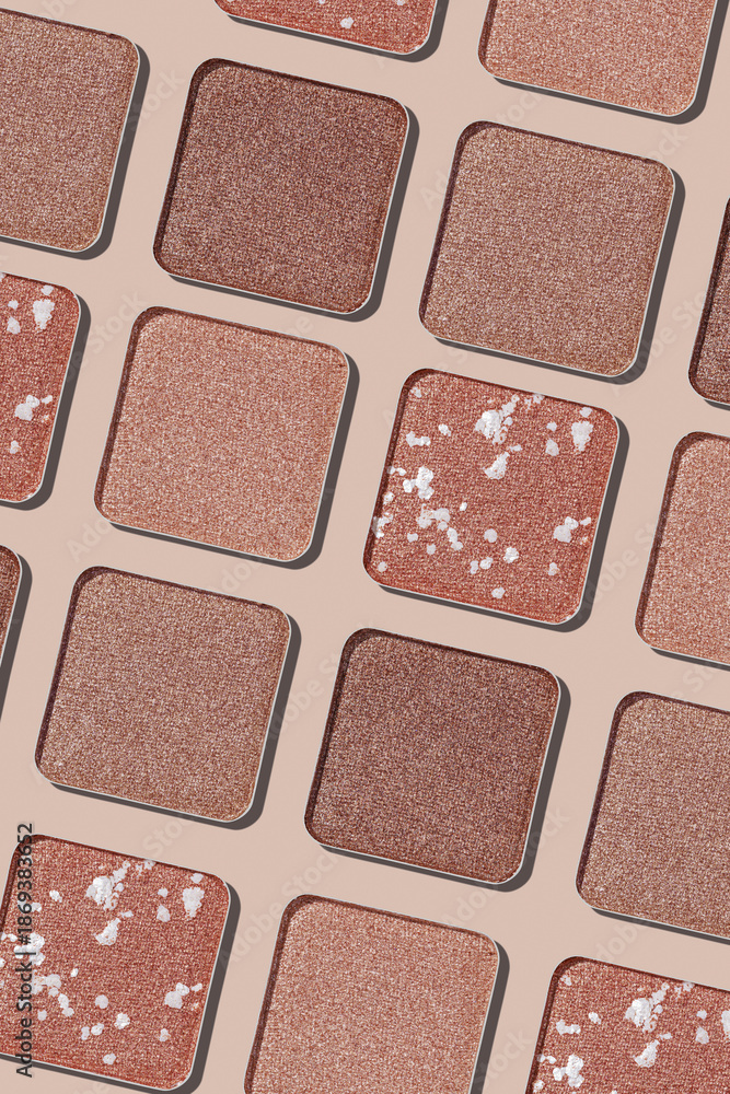 Fototapeta premium Eyeshadow palette background, mix of matte and shimmer shades brown, beige hues. Aesthetic top view pattern for beauty, makeup, cosmetics themes, Neutral colored swatches eyeshade refills
