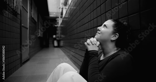 Woman sitting on floor in narrow corridor praying for help during difficult times, hope amid struggle, faith, surrender, emotional vulnerability, spiritual resilience, black and white
