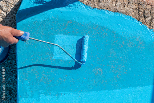 Pintor aplicando revestimento de resina azul numa superfície de piscina com um rolo de lã durante o processo de renovação e manutenção