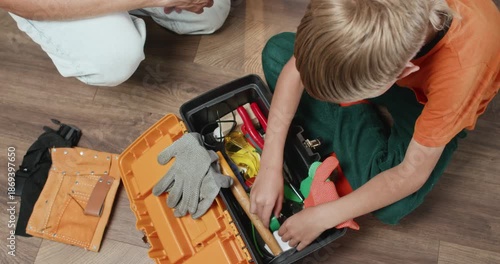 Smart boy searches toolbox to find suitable screwdriver for father during home repair. Moment highlights curiosity and active participation in home repairment