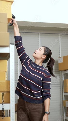 Asian woman small business owner reacting as parcel box falls from shelf, showing accident moment in slow motion during online shopping warehouse work inside vertical workspace