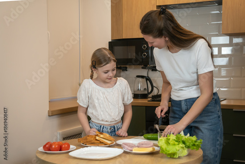 Mother and daughter bonding in a modern kitchen, learning to prepare healthy sandwiches together for breakfast or lunch, smiling and sharing hands-on family cooking time