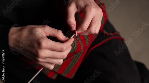 Wallpaper Mural Close-up of a person in a black hoodie knitting with red and green striped yarn, set against a dark background. Focus on hands and fabric. Copy space Torontodigital.ca