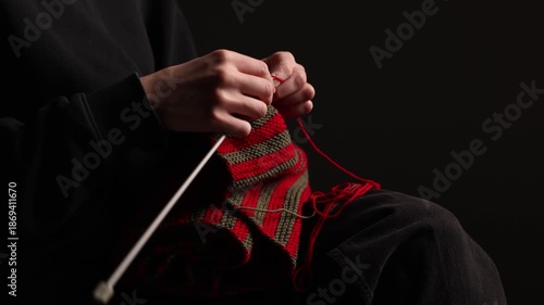 Wallpaper Mural Close-up of a person knitting a red and green striped fabric with needles, seated against a dark background. Focus on yarn and hand movement. Copy space Torontodigital.ca