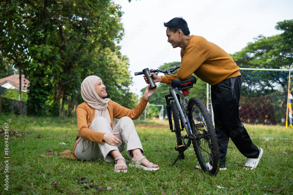 Fototapeta premium Asian couple sharing moment together at the park after cycling and the man handing her a bottle of water.