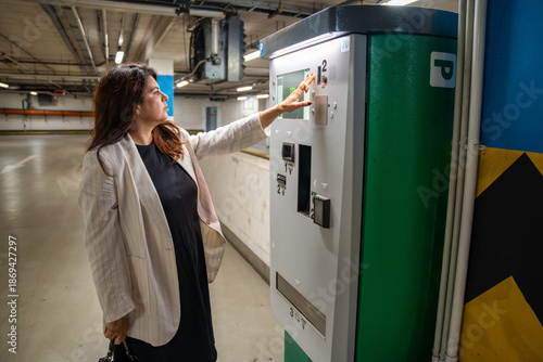 Woman paying for parking at automated payment machine in public parking garage. Everyday urban routine, personal transport management and mobility process in modern city environment