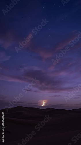 A serene landscape with mountains, moon, clouds, sky, and hills under a dusk sky with vibrant clouds and a low moon.