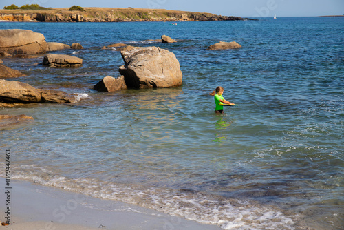Child girl with green t-shirt swimming at Plage de Don beach in Tregung, on the atlantic coast. Finistere, Brittany, France. Profile portrait.