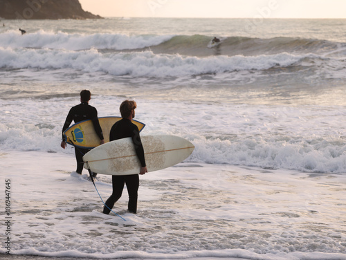 Surfer in warm wetsuit enters water with board at sunset. Winter sports in Italy. Health, sea, and nature.