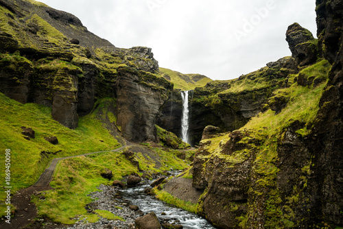 Bild auf Leinwand Hidden waterfall cascading down a lush green mossy canyon in Iceland