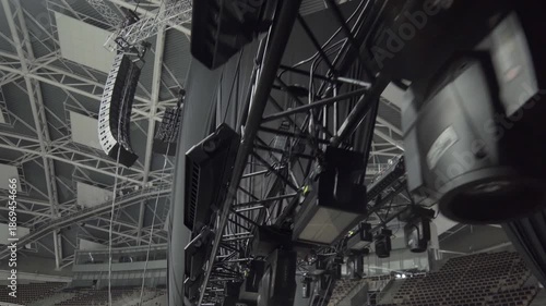 Lighting equipment hangs from overhead truss structure. Black fixtures align in row preparing stage illumination for upcoming concert