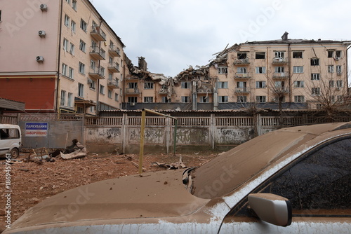 The building damaged by a direct missile hit. The courtyard and cars are covered in debris. An apocalyptic atmosphere.