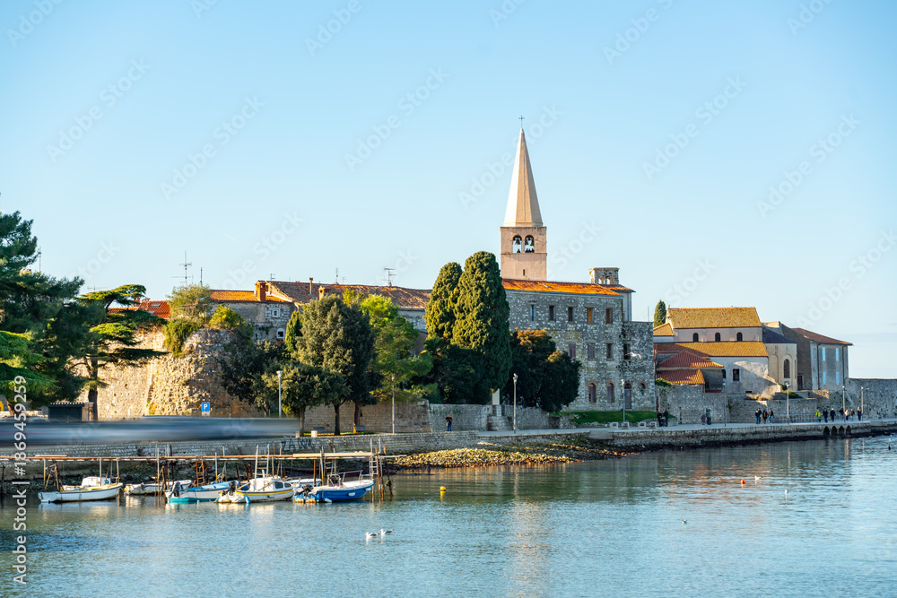 Obraz premium Scenic view of Poreč old town with historic buildings, church tower and small marina along the Adriatic Sea on a sunny day at winter